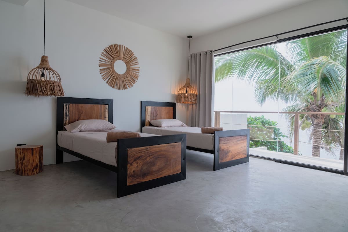 A modern bedroom with two beds, a large window with a view of palm trees, and decorative wall art.