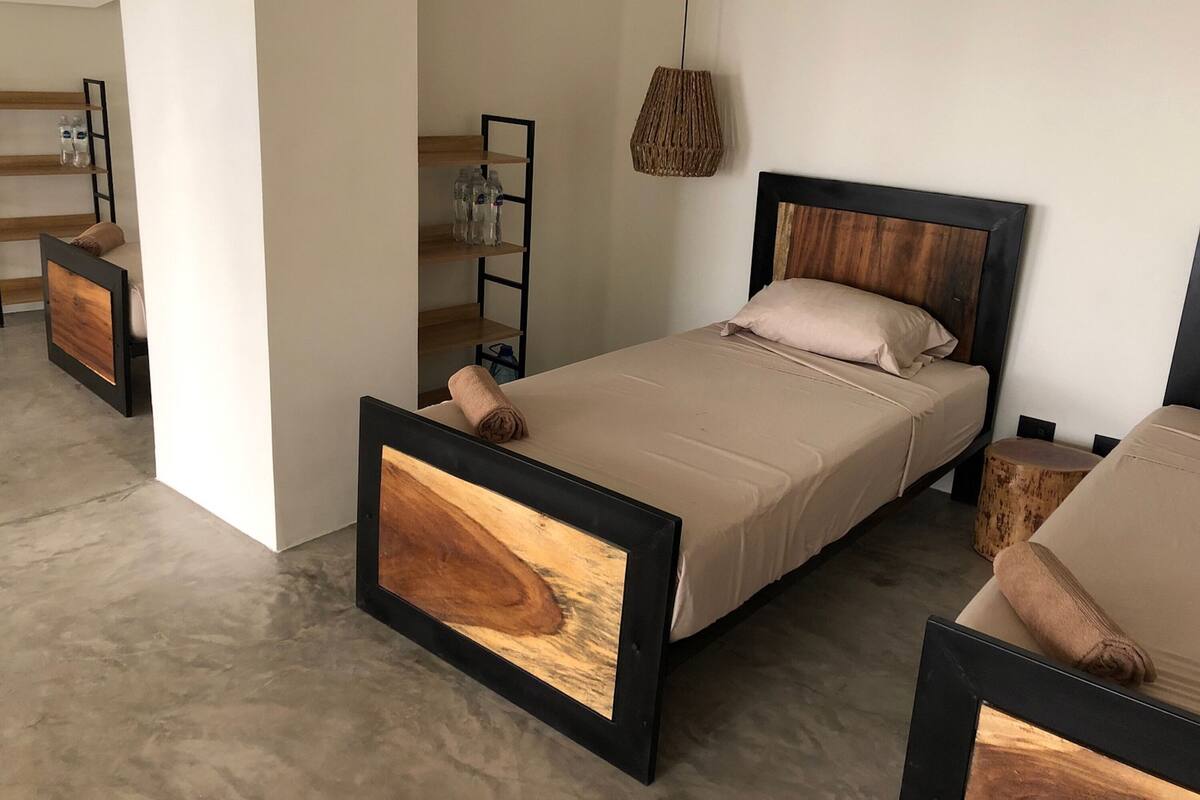 A modern bedroom with a wooden bed frame, a bedside table, a hanging light, and a built-in shelf with bottles.