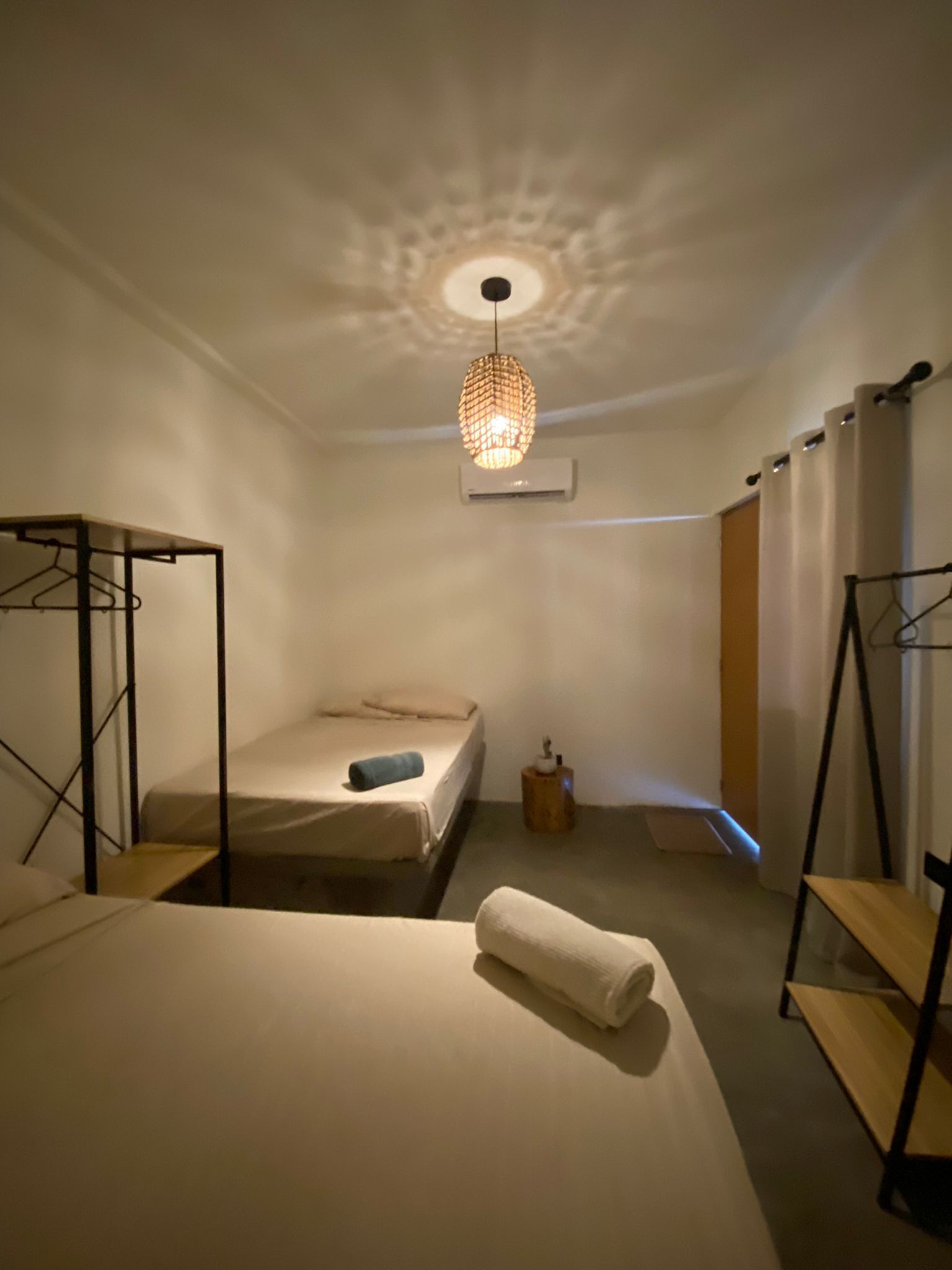 A small, well-lit bedroom with a single bed, a hanging light fixture, and a wardrobe.