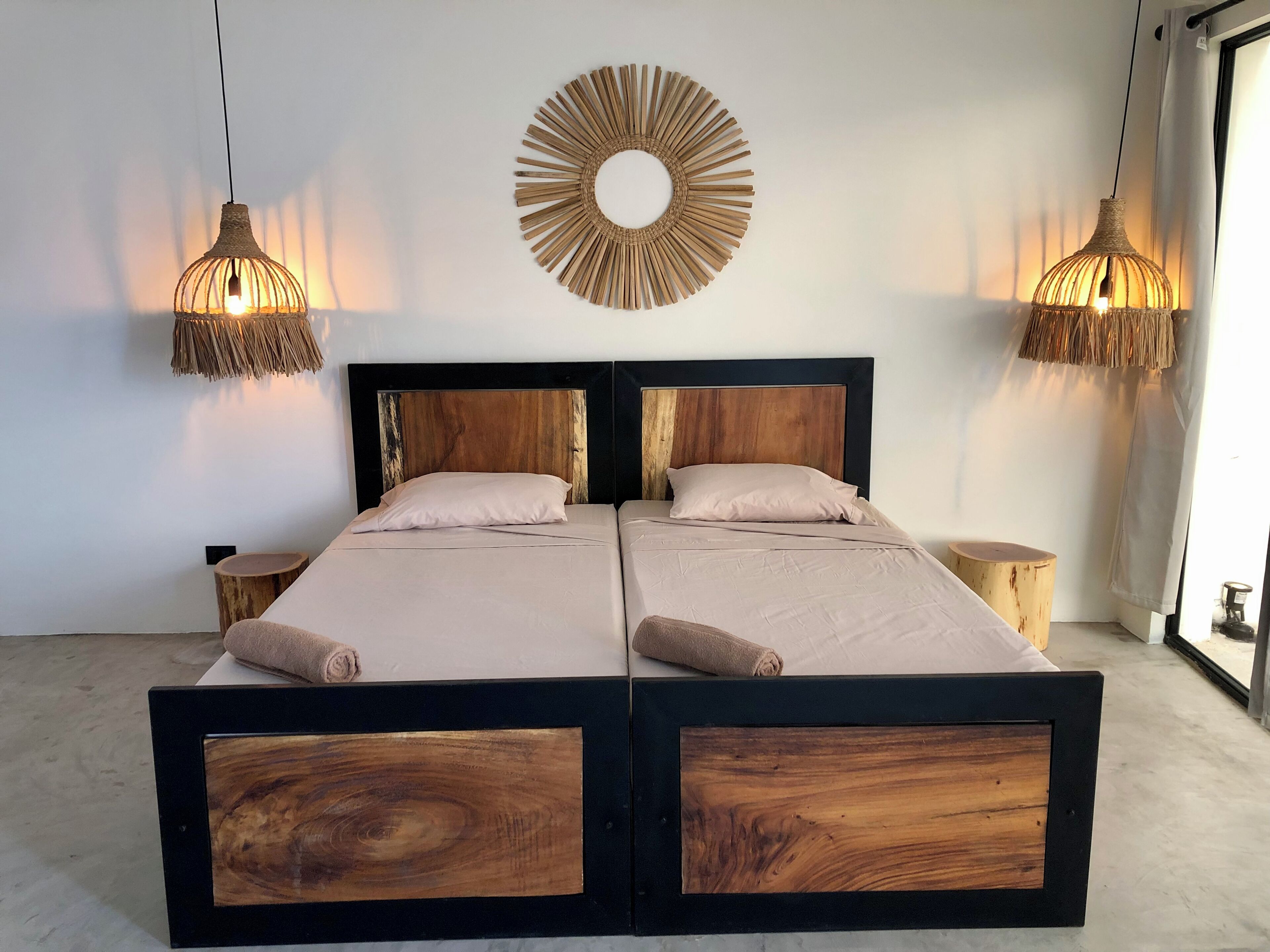 A double bed with a wooden frame and headboard, two bedside tables, a round wall decoration, and hanging lamps.