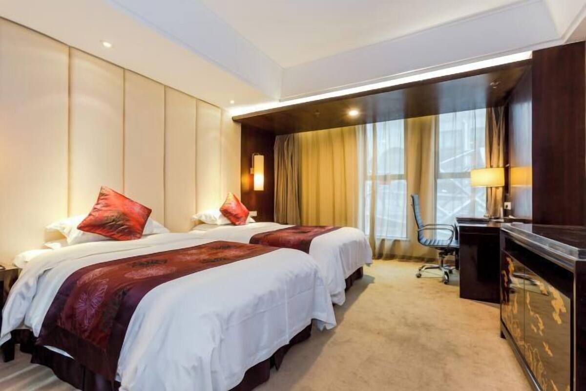 Een hotelkamer met twee bedden, een bureau, een stoel en een groot raam met gordijnen.