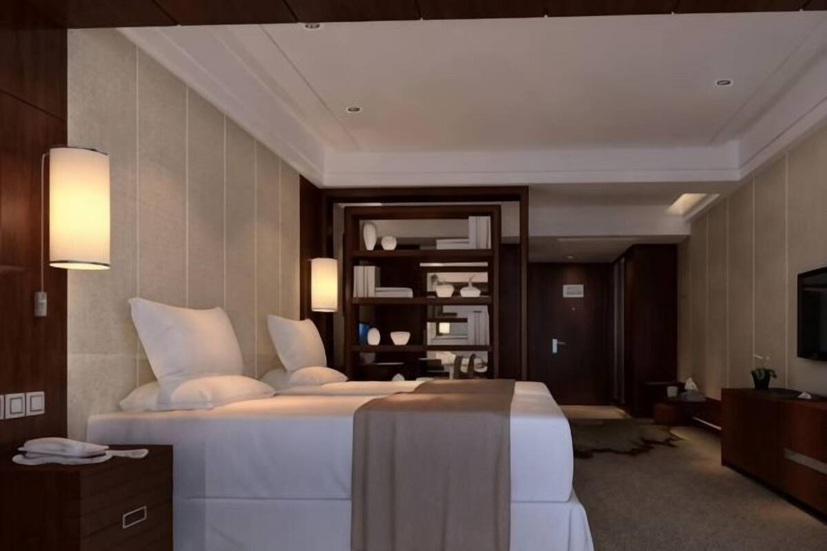 Een hotelkamer met een bed, nachtkastjes, een televisie, een boekenplank en een deur naar een andere kamer.
