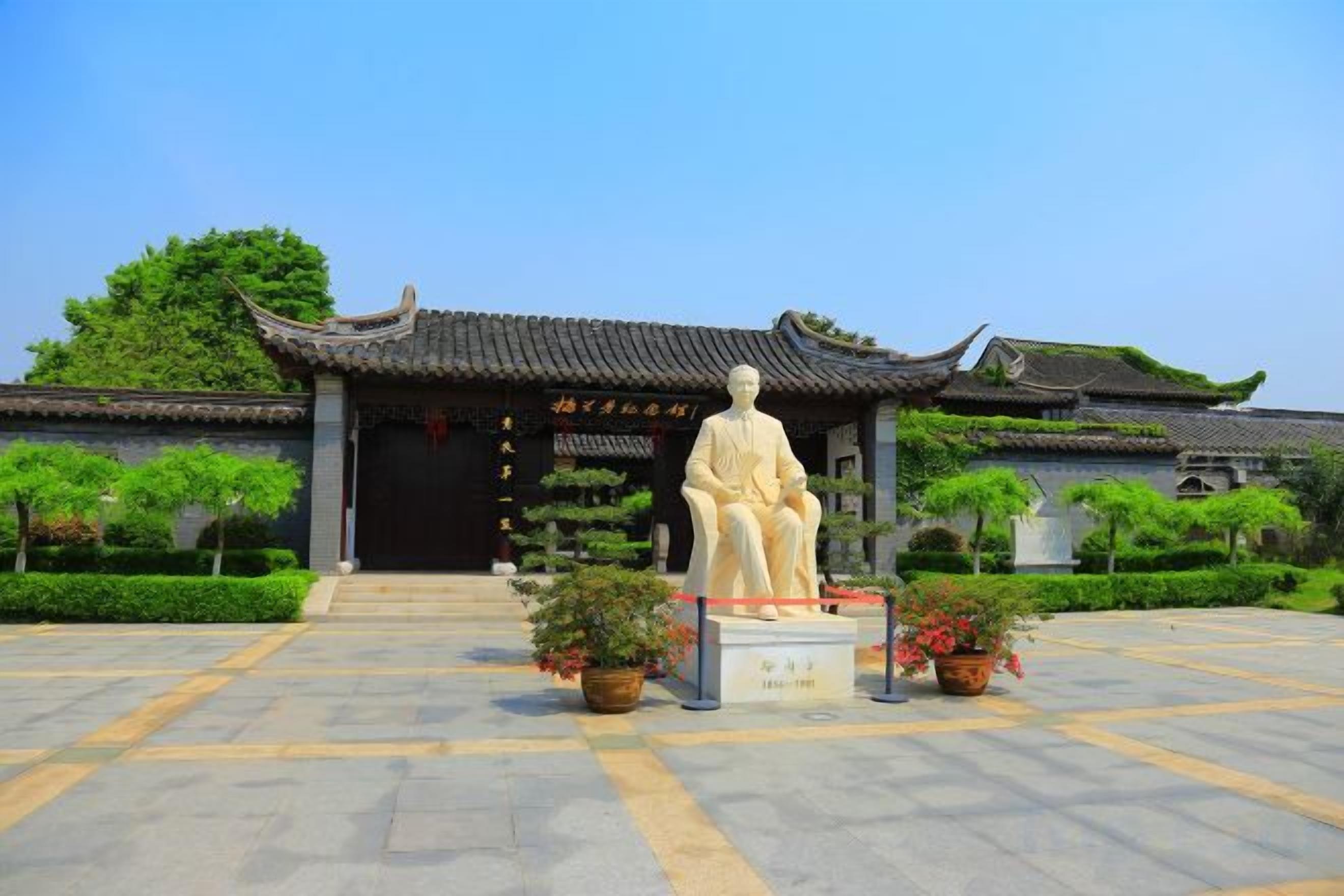 A traditional building with a statue in front, a tiled entrance, and well-maintained landscaping.