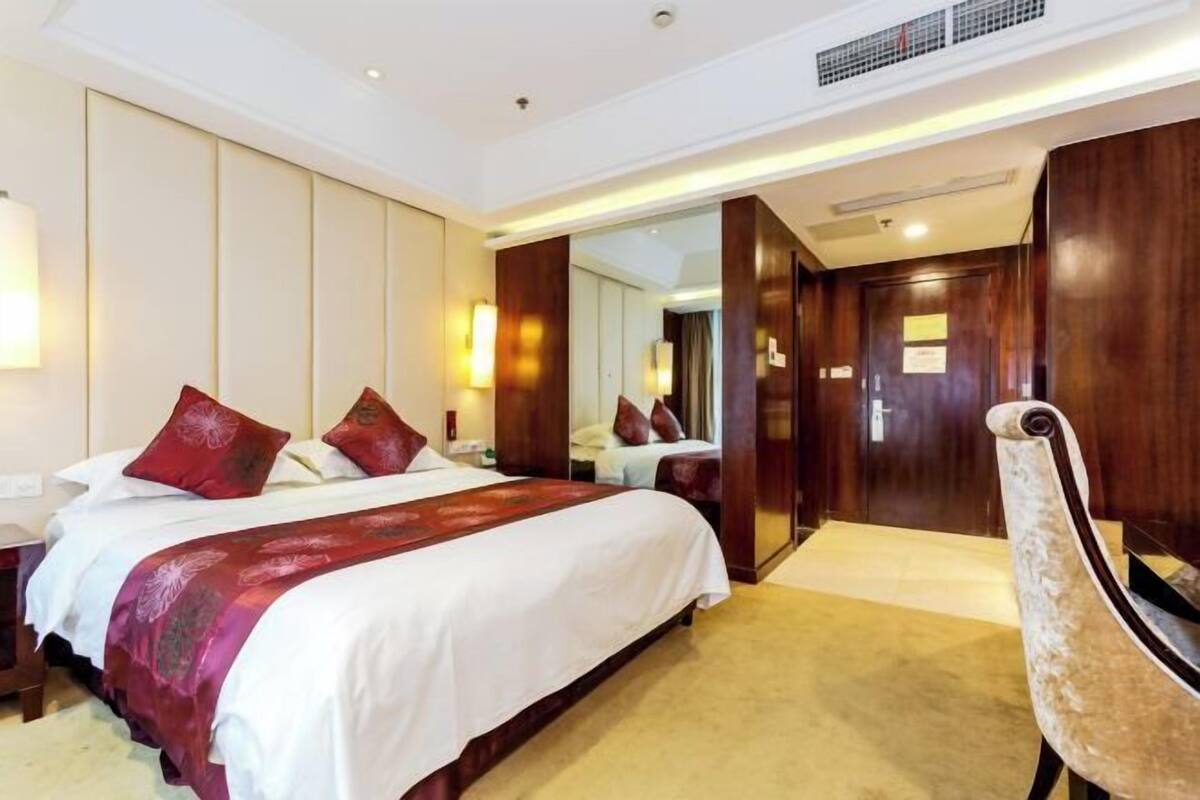 Een hotelkamer met een groot bed, een houten garderobe, een spiegel en een stoel.
