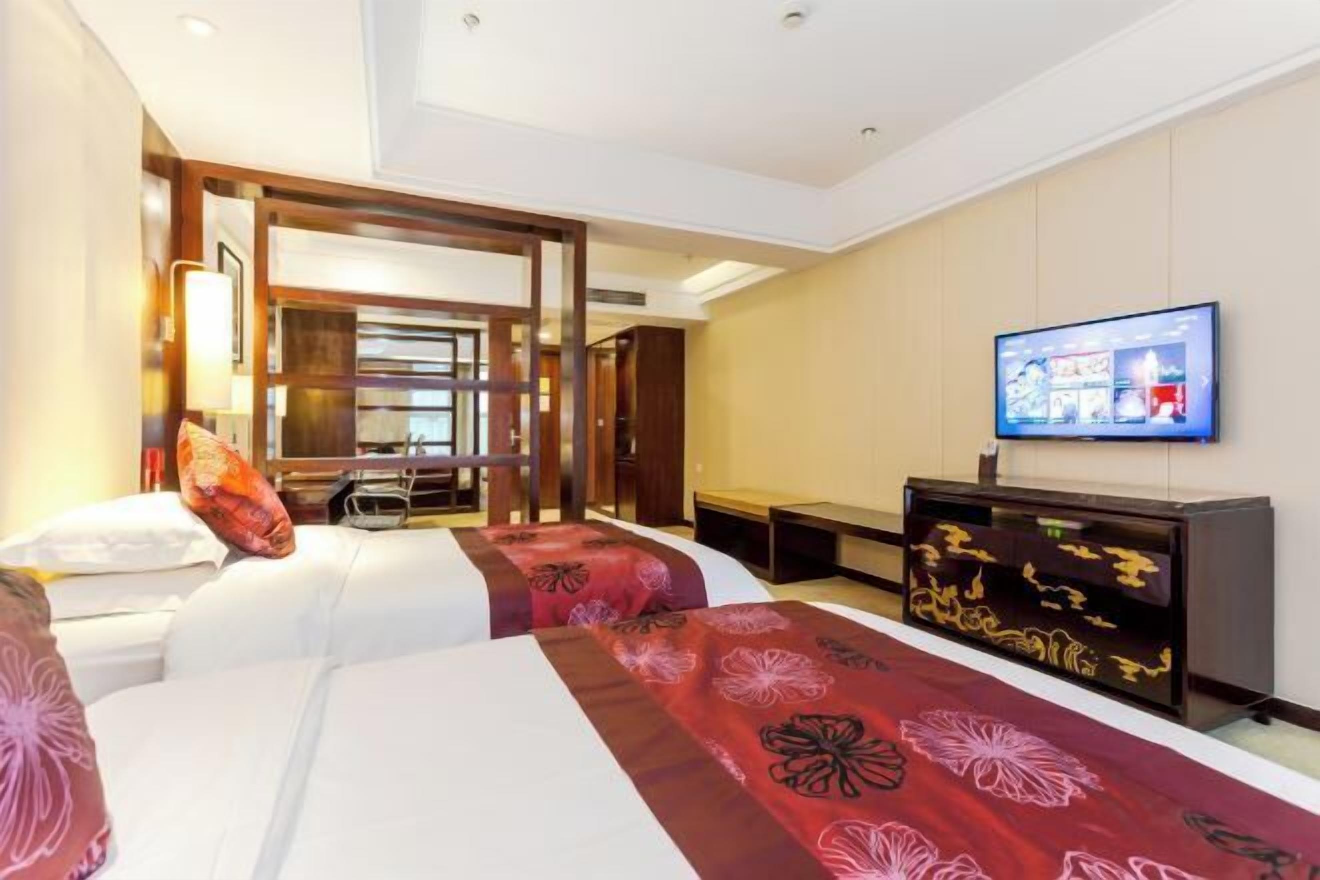 A hotel room with two beds, a TV, and a desk.