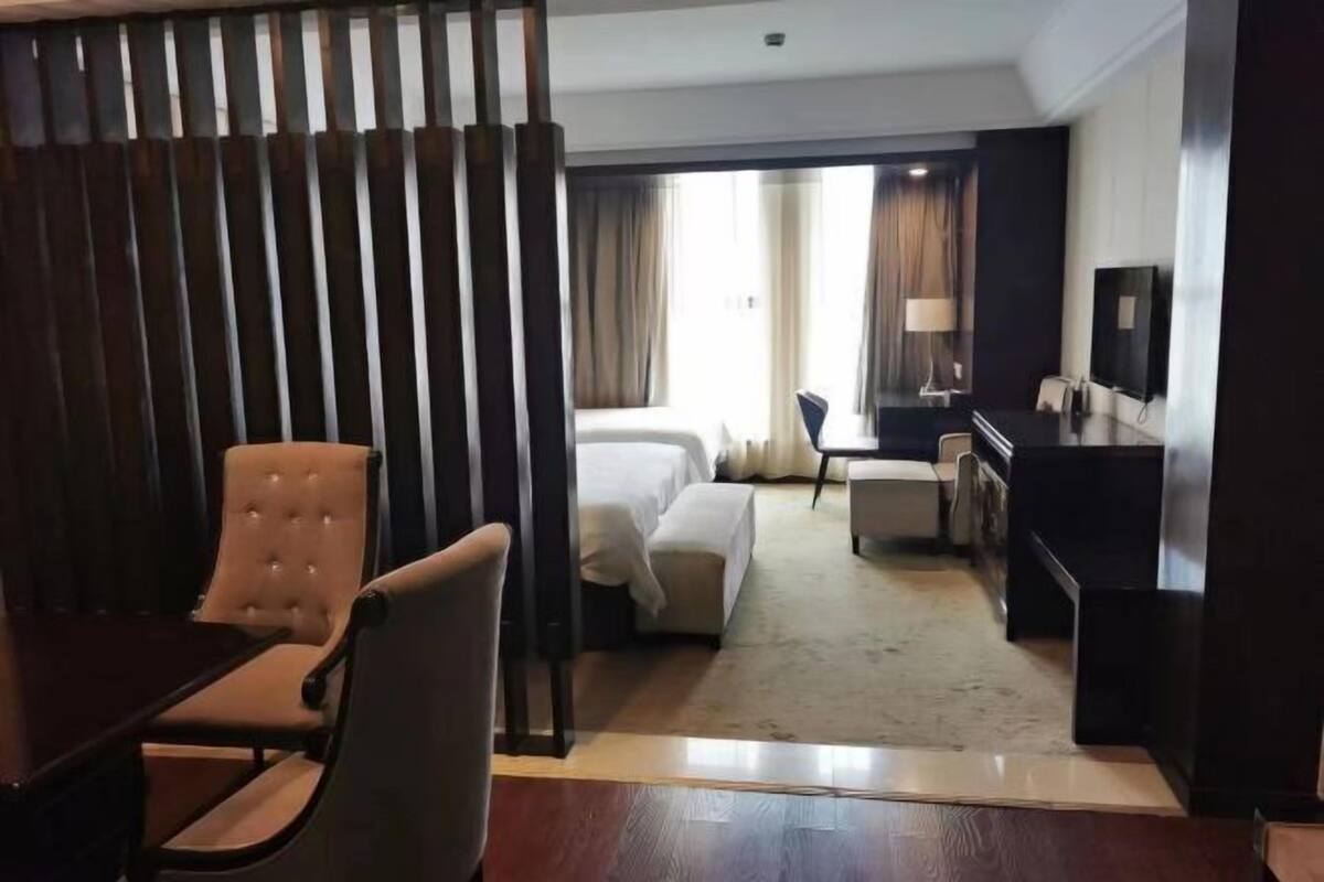 Een hotelkamer met een bed, een bureau, een stoel, een televisie en een raam met gordijnen.