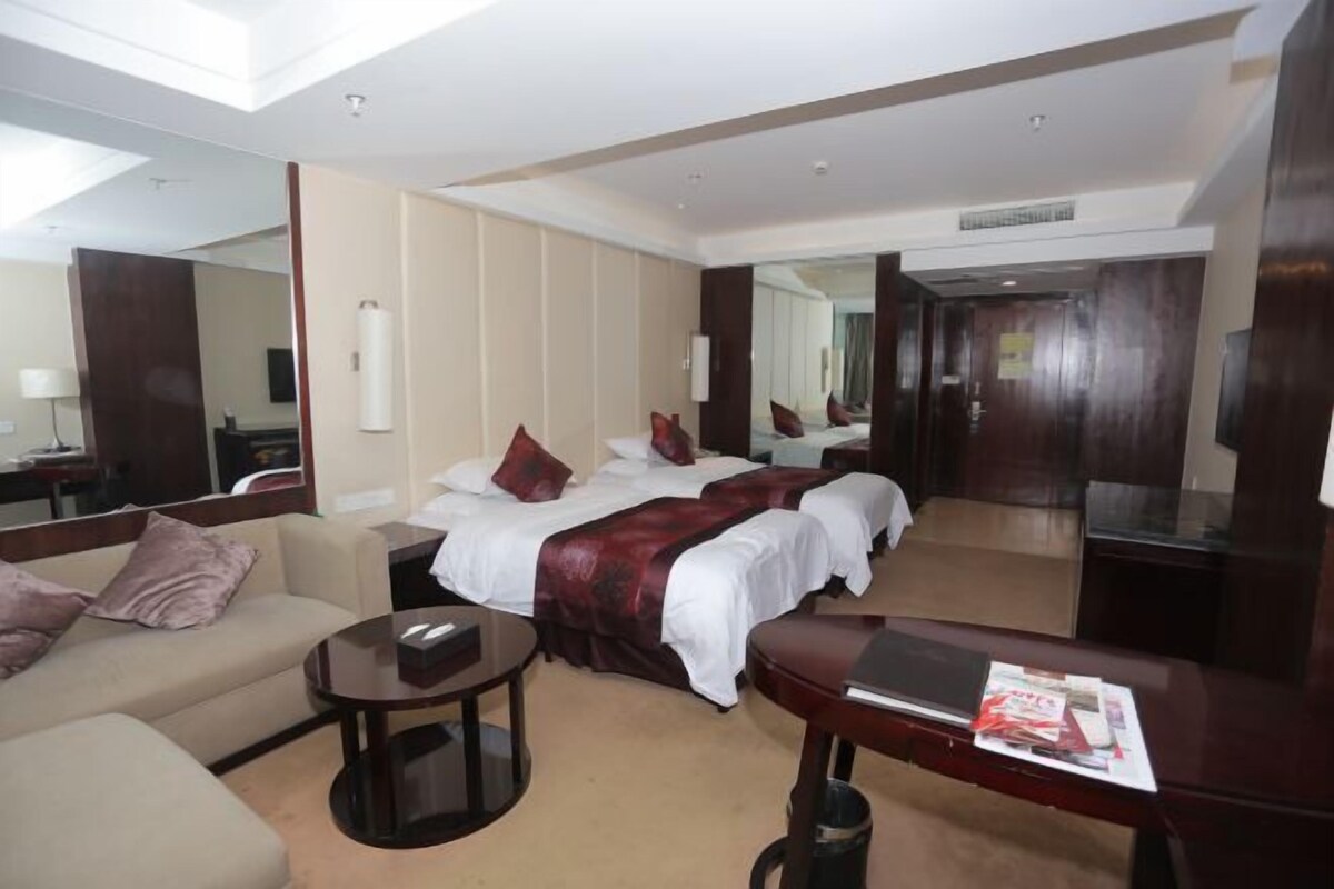 A hotel room with a bed, a sofa, a coffee table, and a desk with a laptop and magazines.