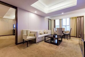 Ein modernes Hotelzimmer mit einer Couch, Sesseln, einem Couchtisch und einem Essbereich mit Stühlen und einem Tisch.