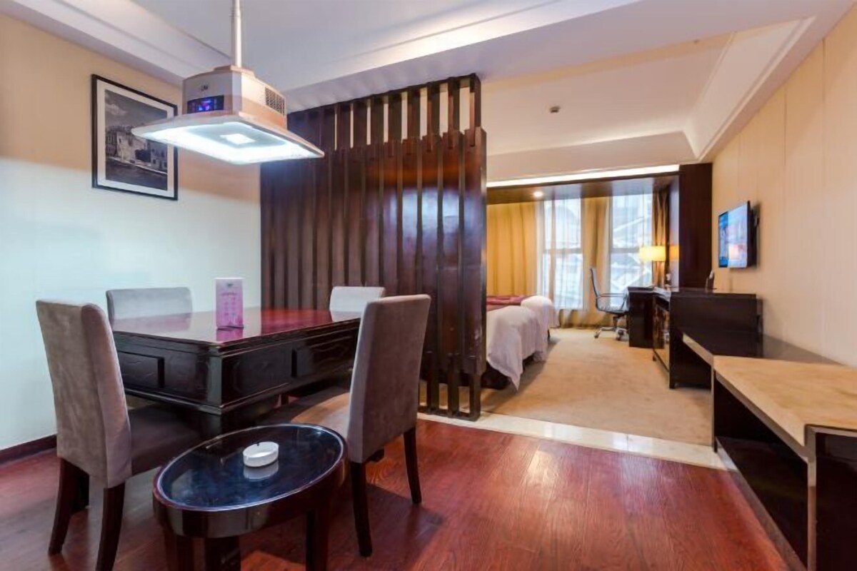 A hotel room with a dining table, chairs, a bed, a TV, and a large window.