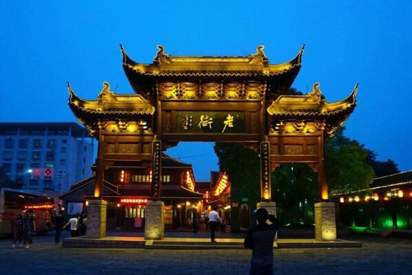 Une porte chinoise traditionnelle, agrémentée d’enseignes lumineuses, une zone d’entrée pavée et un bâtiment en arrière-plan.