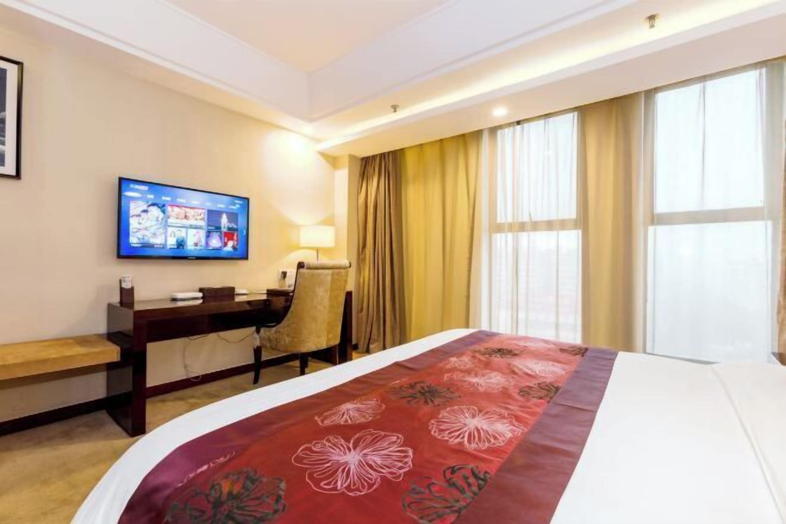 Une chambre d’hôtel avec un grand lit, un bureau avec une chaise, une télévision et une fenêtre avec des rideaux.