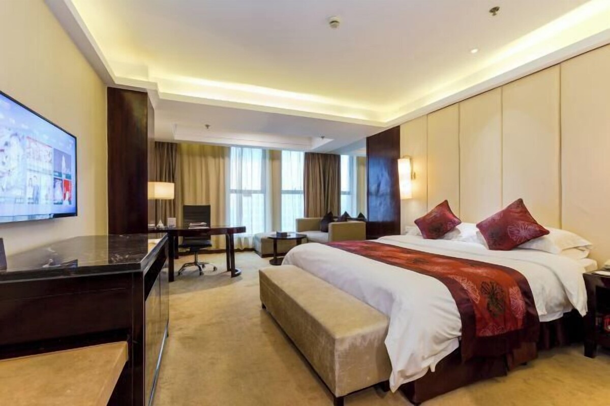 A hotel room with a large bed, a desk, a chair, and a TV on the wall.