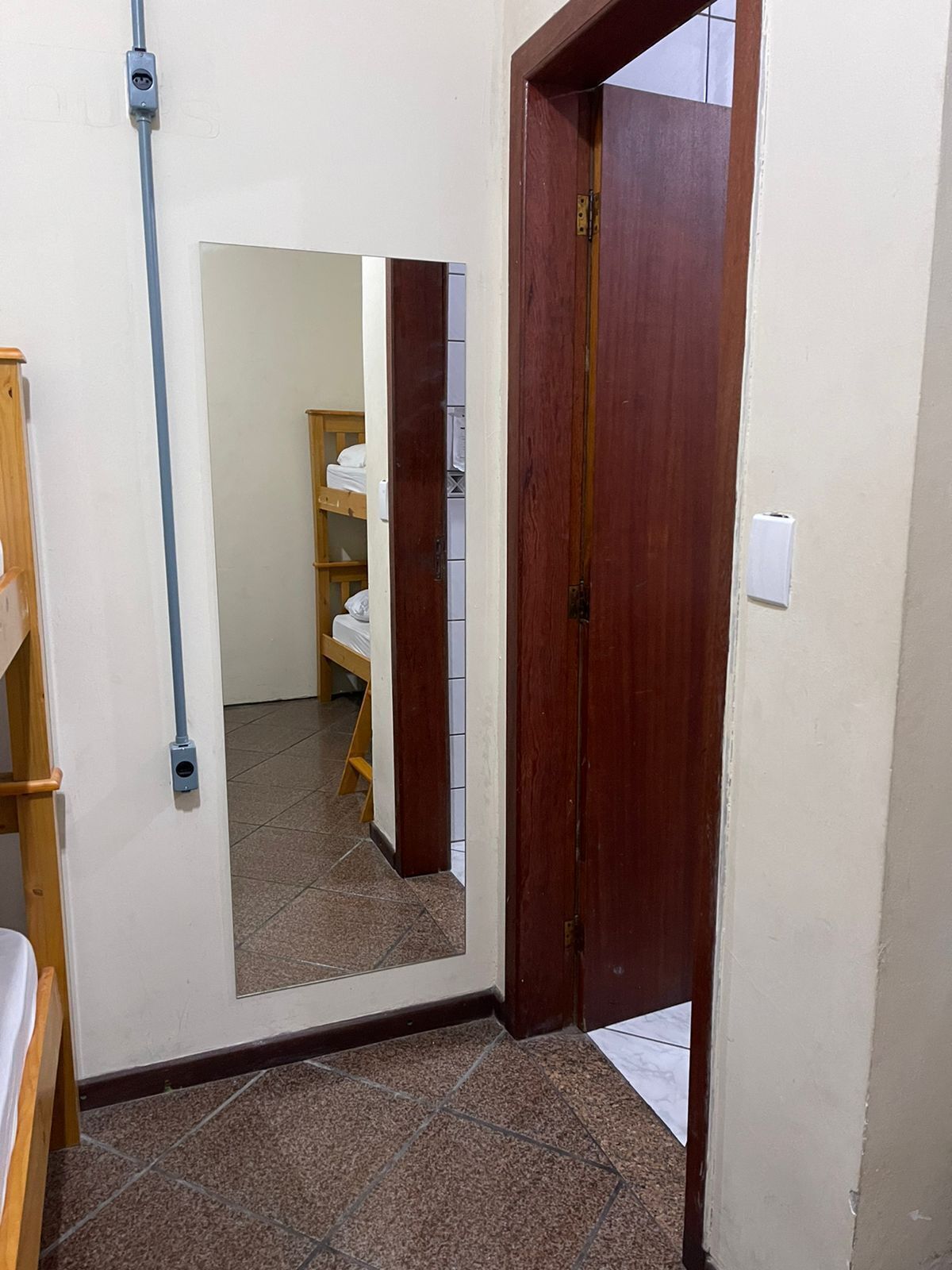A narrow hallway with a wooden door, a mirror, and a tiled floor.