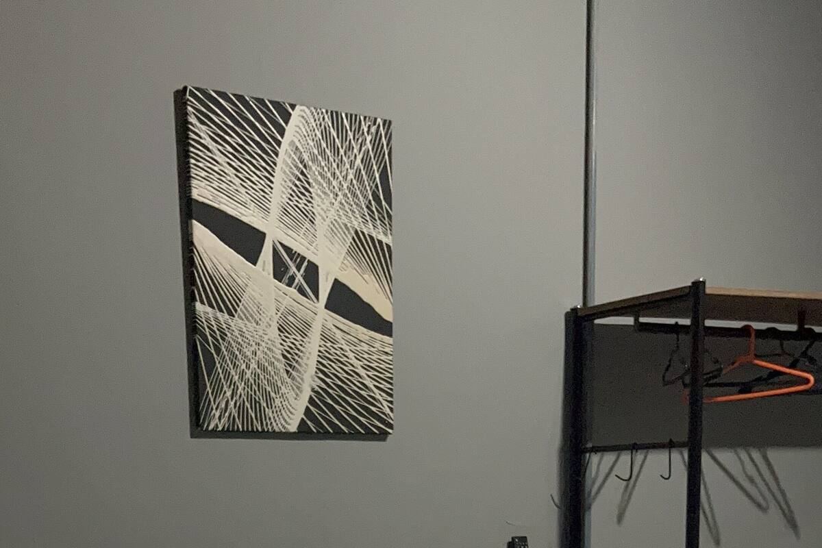 Ein Bett mit weißer und blauer Bettwäsche, einem Holz-Kopfteil und einem an der Wand hängenden abstrakten Kunstwerk.