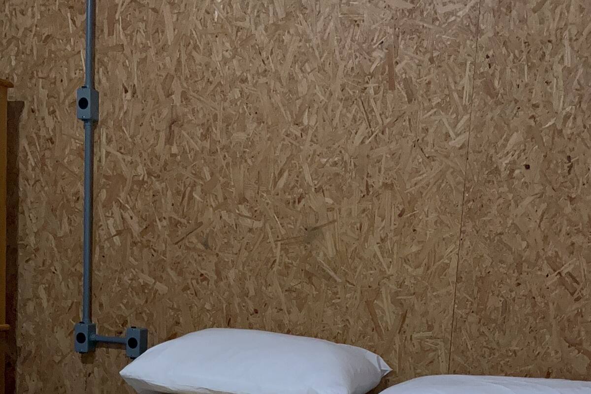 Ein Zimmer mit einer Holzwand, einer Metallrohrleitung und zwei weißen Kissen auf einem Bett.