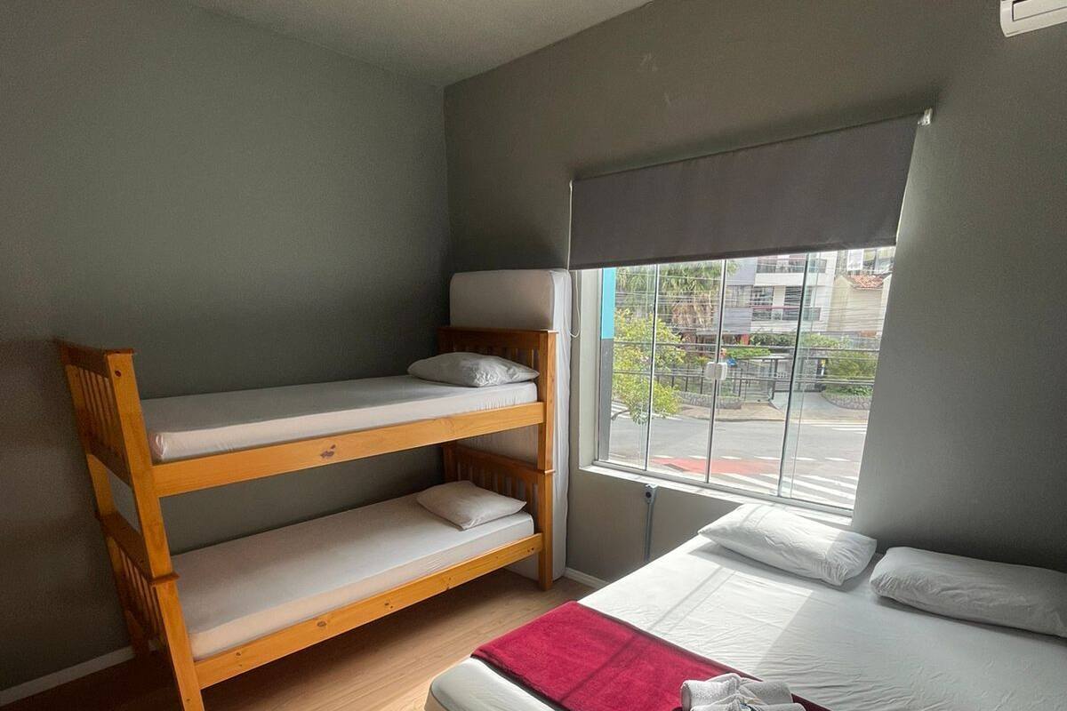 Ein Zimmer mit einem Etagenbett, einem Einzelbett, einem Fenster mit Blick auf Gebäude und einer Deckenleuchte.