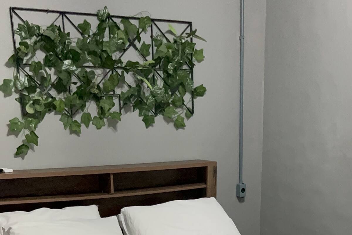 Ein Bett mit weißen Leinen und einer grauen Decke, ein Holz-Kopfteil und eine hängende Zimmerpflanze.