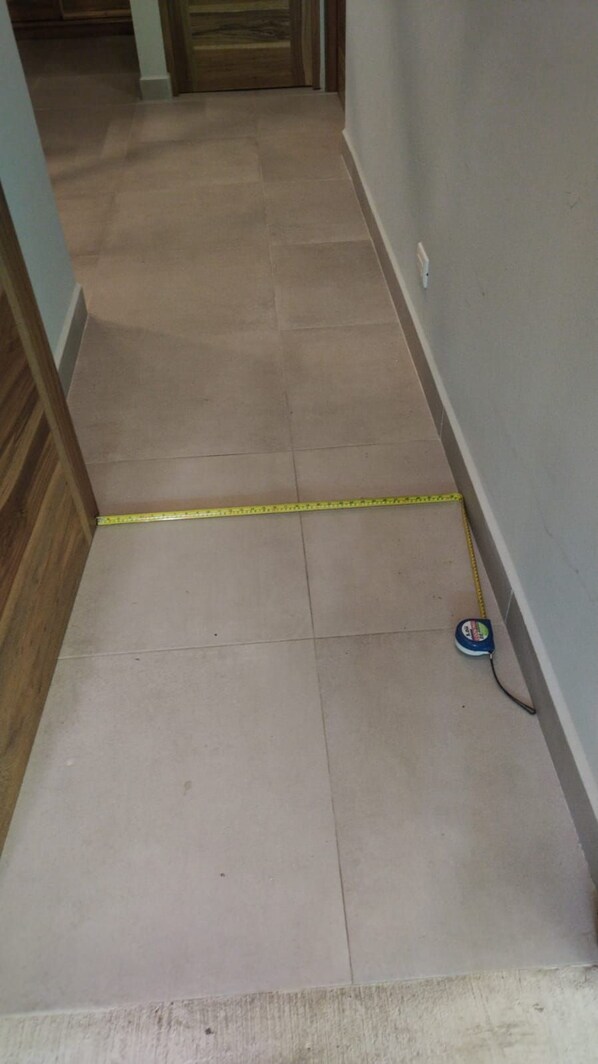 A hallway with a yellow measuring tape on the floor, a blue object on the right, and a wooden door at the end.