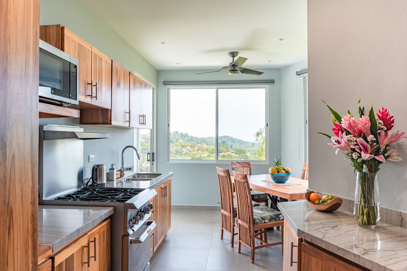 A modern kitchen with wooden cabinets, stainless steel appliances, and a large window offering a view of the landscape.