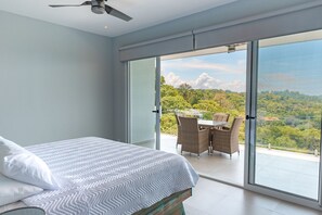A bedroom with a bed, a ceiling fan, and a balcony with a table and chairs.