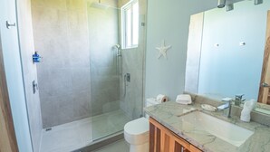 A modern bathroom with a glass-enclosed shower, a marble sink, and a large mirror. - 🌅 Panoramic Ocean View Penthouse Suite at Villa Costa Vida (Quepos)