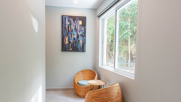 A modern interior with a large window, two wicker chairs, a small table, and a colorful abstract painting on the wall. - 🌅 Ocean-View 2-Bedroom Suite #2 at Villa Costa Vida (Quepos)