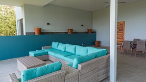 A covered outdoor seating area with a large sectional sofa, a small table, and a dining table with chairs. - 🌅 Ocean-View 2-Bedroom Suite #2 at Villa Costa Vida (Quepos)