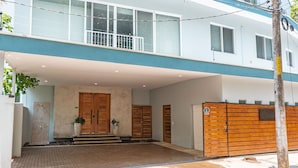 A modern two-story house with a large wooden gate, a covered entrance with steps, and a balcony.