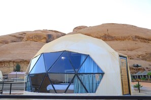 A geodesic dome tent with a bed inside, set against a desert landscape with rocky hills in the background. - Albasha camp wadi rum (Wadi Rum)