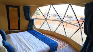 Une chambre avec une grande fenêtre, un lit, une porte en bois et une vue sur les voitures garées à l’extérieur.
