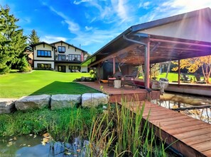 A modern house with a covered patio, a pond, and a well-maintained lawn. - Luxurious Waterfront Villa & Cottage House, Niagara Falls, Ontario (Niagara Falls)