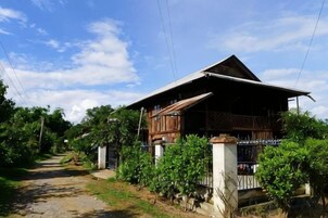 Una casa de madera con techo inclinado, rodeada de vegetación y un sendero de tierra.