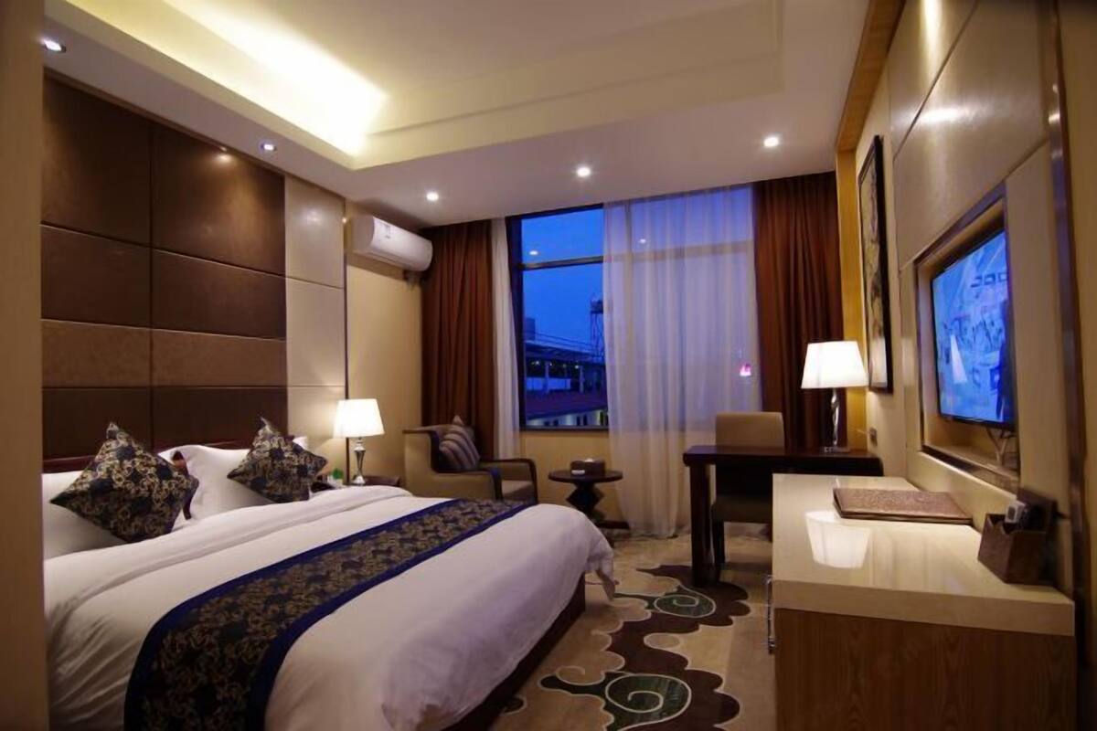 A hotel room with a large bed, a desk, a TV, and a window with curtains.