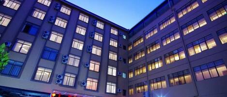 A multi-story hotel building with a central courtyard, large windows, and a visible entrance with a red awning.