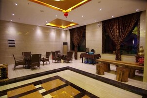 Um saguão de hotel com área de estar central, uma janela grande com cortinas e uma luminária decorativa no teto.