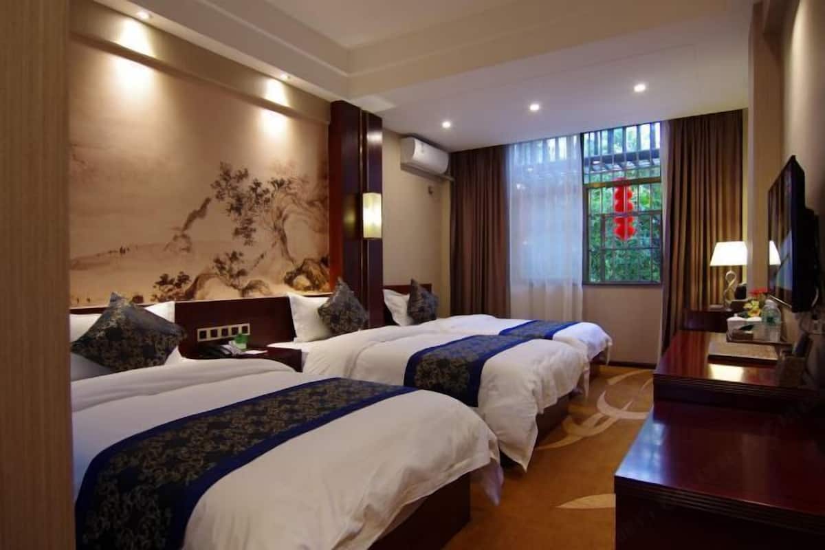 A hotel room with two beds, a large wall mural, a window with curtains, and a desk with a lamp.