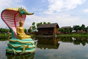 A Buddha statue on a dragon sculpture by a calm water body with traditional buildings in the background.