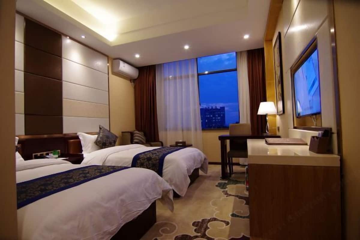 A hotel room with two beds, a desk, a chair, a TV, and a window with a city view.