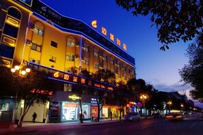 A hotel with multiple floors, a prominent sign, and a street in front with shops and parked cars. - Biancheng Hotel (Ruili)