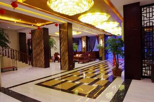 A hotel lobby with a checkered floor, large chandeliers, and a staircase.