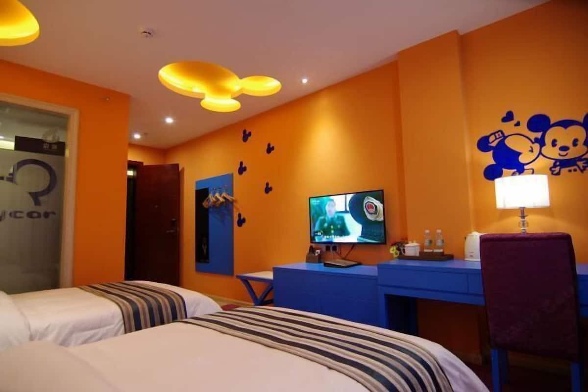 A hotel room with two beds, a desk with a computer, a TV, and a wall with cartoon characters.