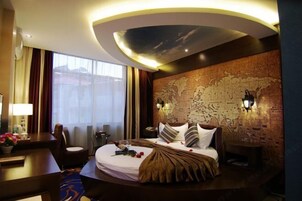 Quarto de hotel com uma cama grande, uma escrivaninha com luminária, um mapa na parede e vista para o exterior pela janela.