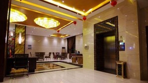 A hotel lobby with a reception desk, seating area, and an elevator. - Biancheng Hotel (Ruili)