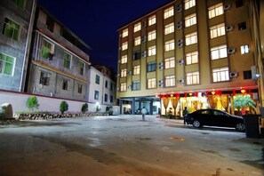 A hotel with multiple floors, a parking area, and a building with a red awning. - Biancheng Hotel (Ruili)