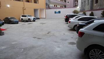 A parking area with several cars parked in rows, a building entrance, and a staircase leading to an upper level.