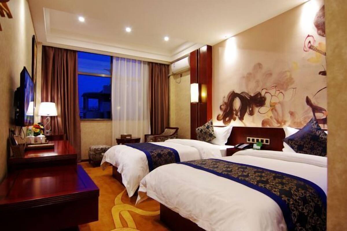 A hotel room with two beds, a desk, a TV, and a window with curtains.