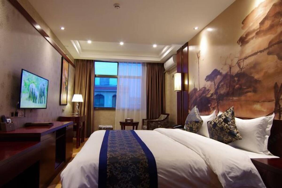 A hotel room with a large bed, a desk, a television, and a painting on the wall.