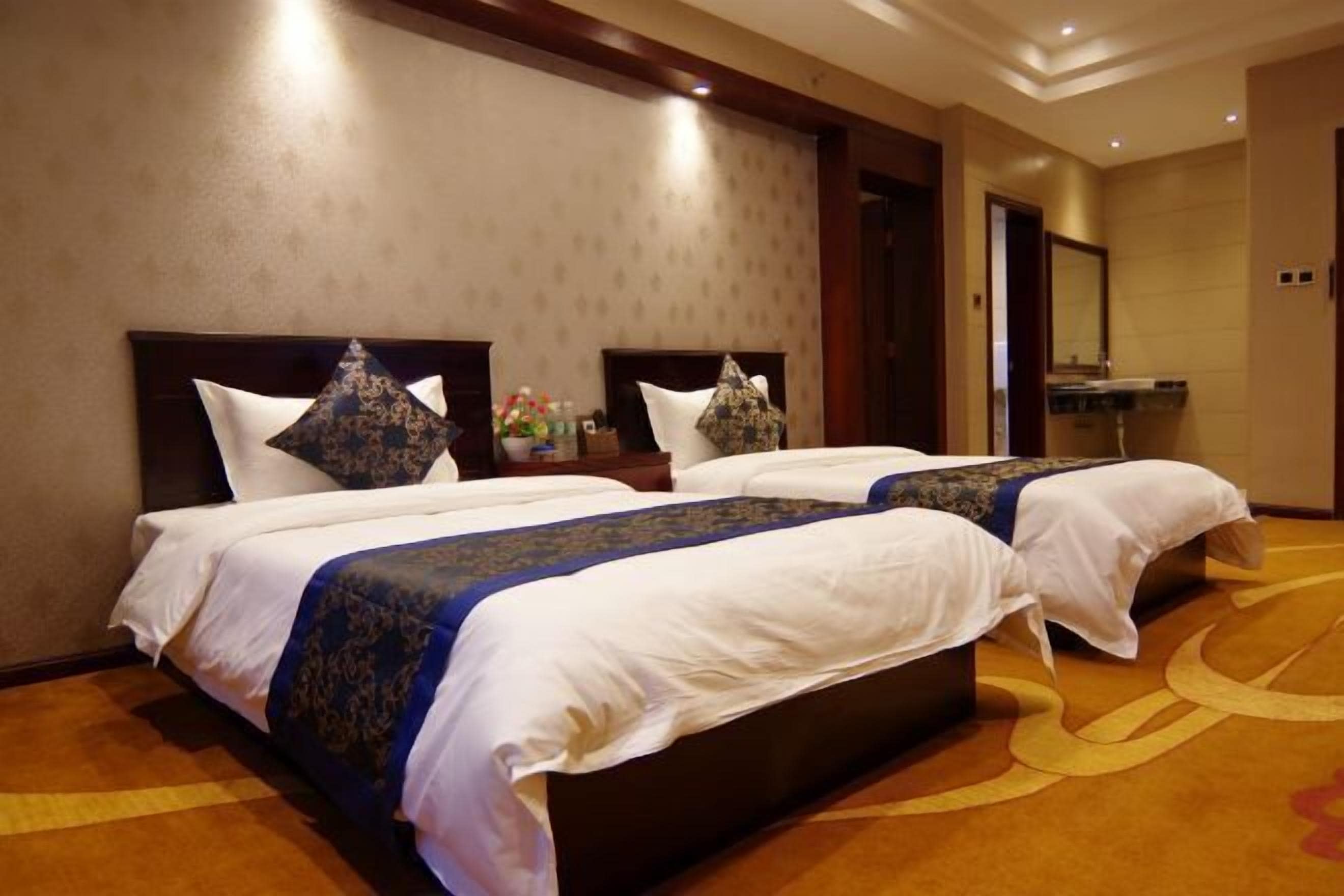 A hotel room with two beds, a nightstand, a mirror, and a bathroom visible through an open door.