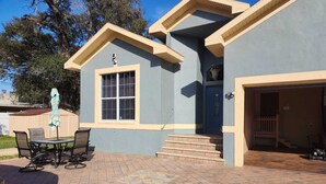 A two-story house with a blue exterior and beige trim, a front porch with a table and chairs, and a garage.