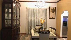 A dining area with a table set for four, a dark wooden cabinet, a chandelier, and a framed picture on the wall.
